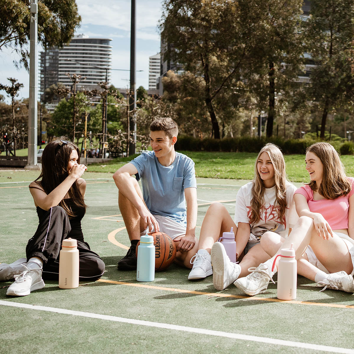 A group of young adults sitting on a basketball court with insulated drink bottles.